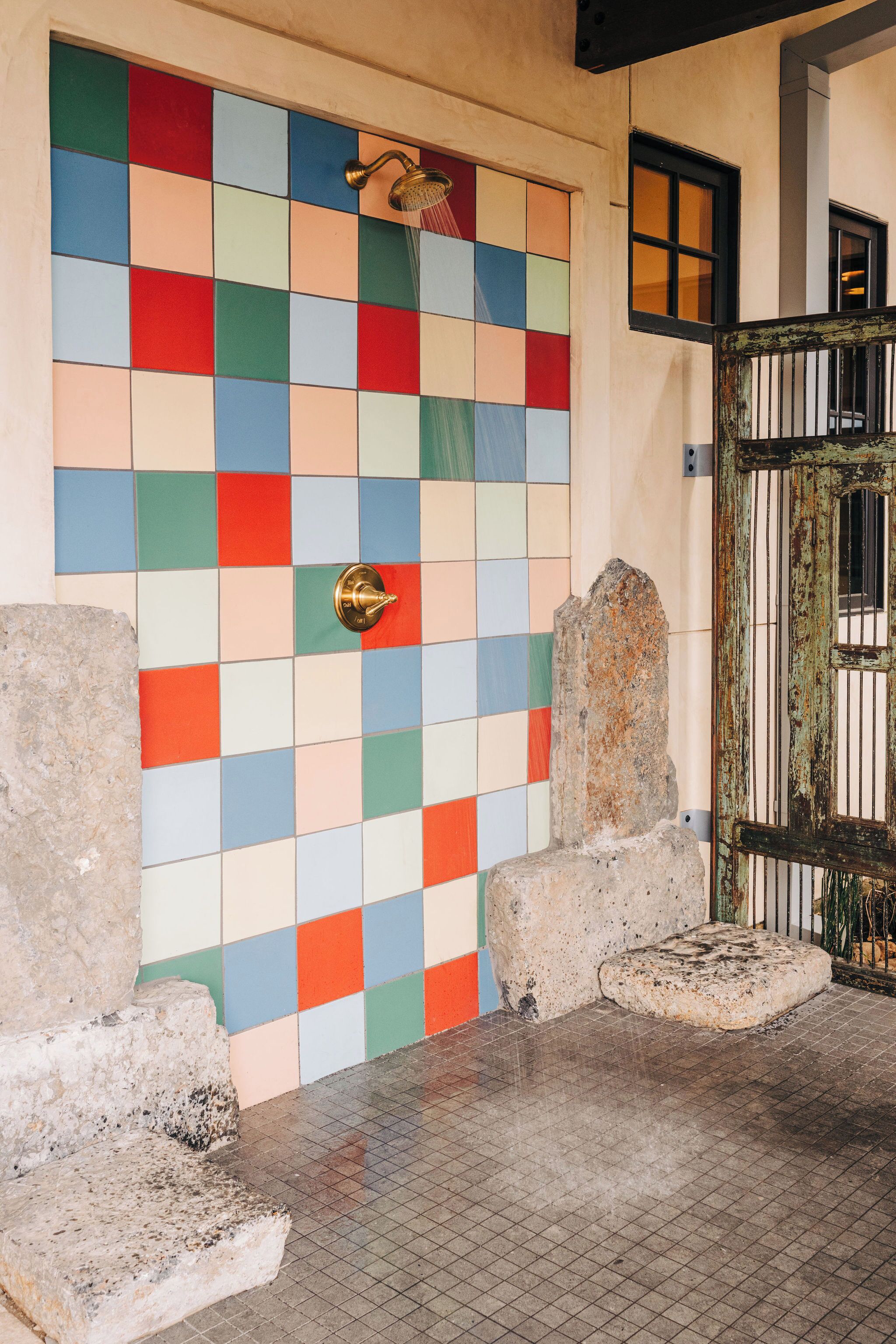 Un mur recouvert de carreaux colorés, avec une pomme de douche, une porte rustique et des marches en pierre.