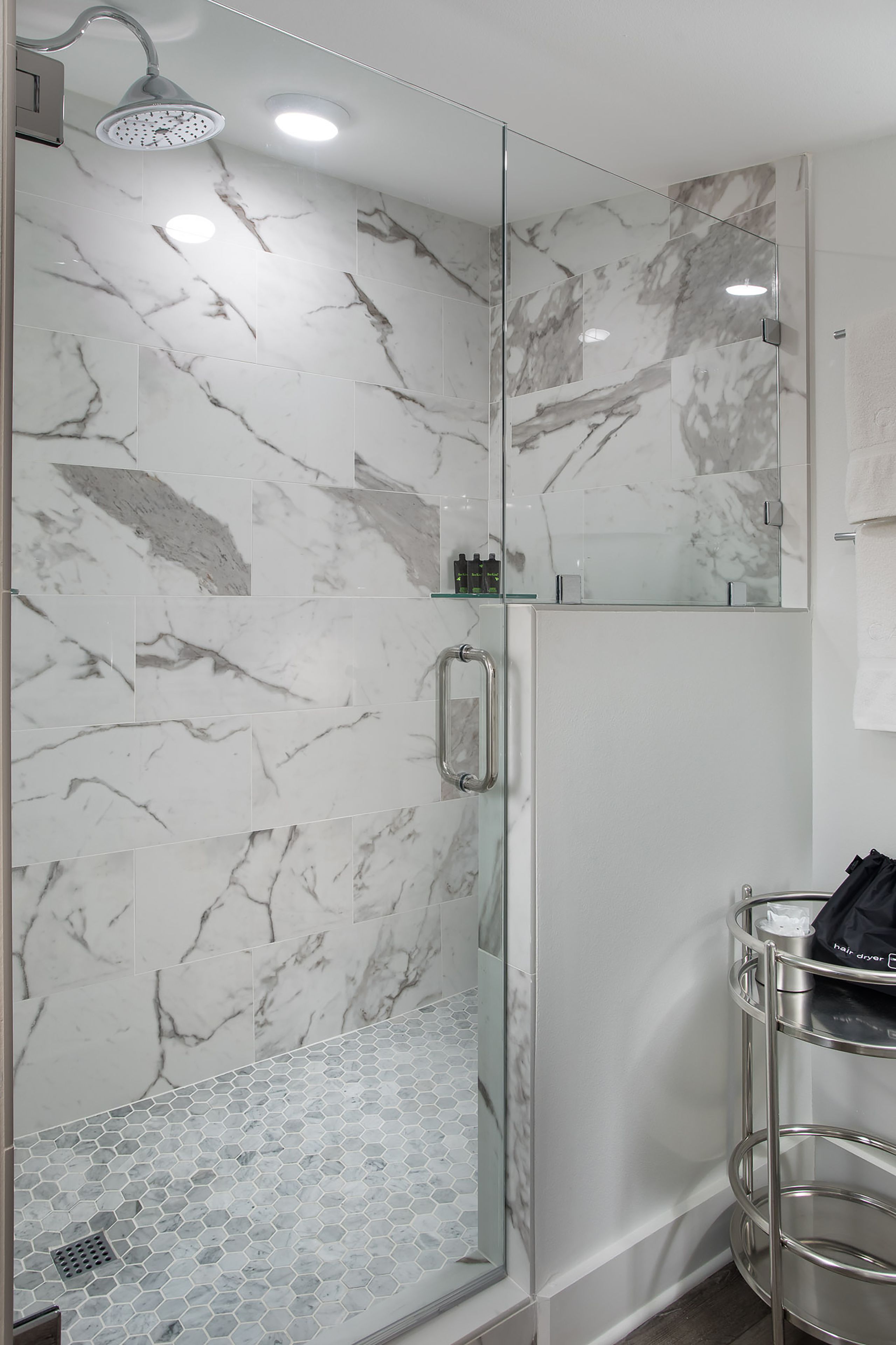 A modern bathroom with marble walls, a glass shower enclosure, and a metal vanity.