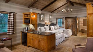 A cozy bedroom with a large bed, wooden cabinetry, a desk, and a view of the outdoors. - Camp Lucy (Dripping Springs)