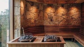 A stone-walled sauna with wooden benches and a wooden table with baskets. - Camp Lucy (Dripping Springs)