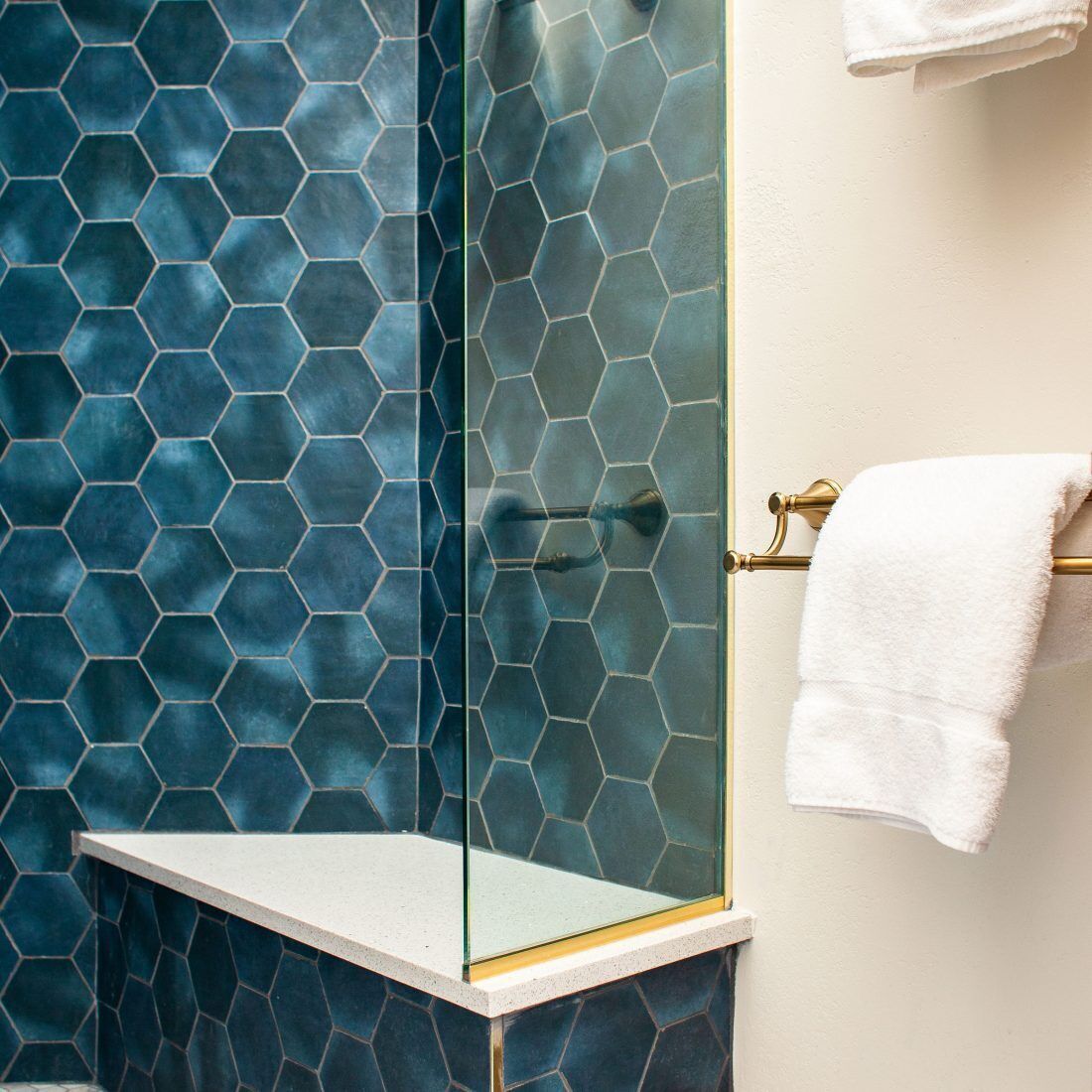 Un bagno con box doccia in vetro, portasciuga asciugamani bianco e un rivestimento a mosaico esagonale sulle pareti.