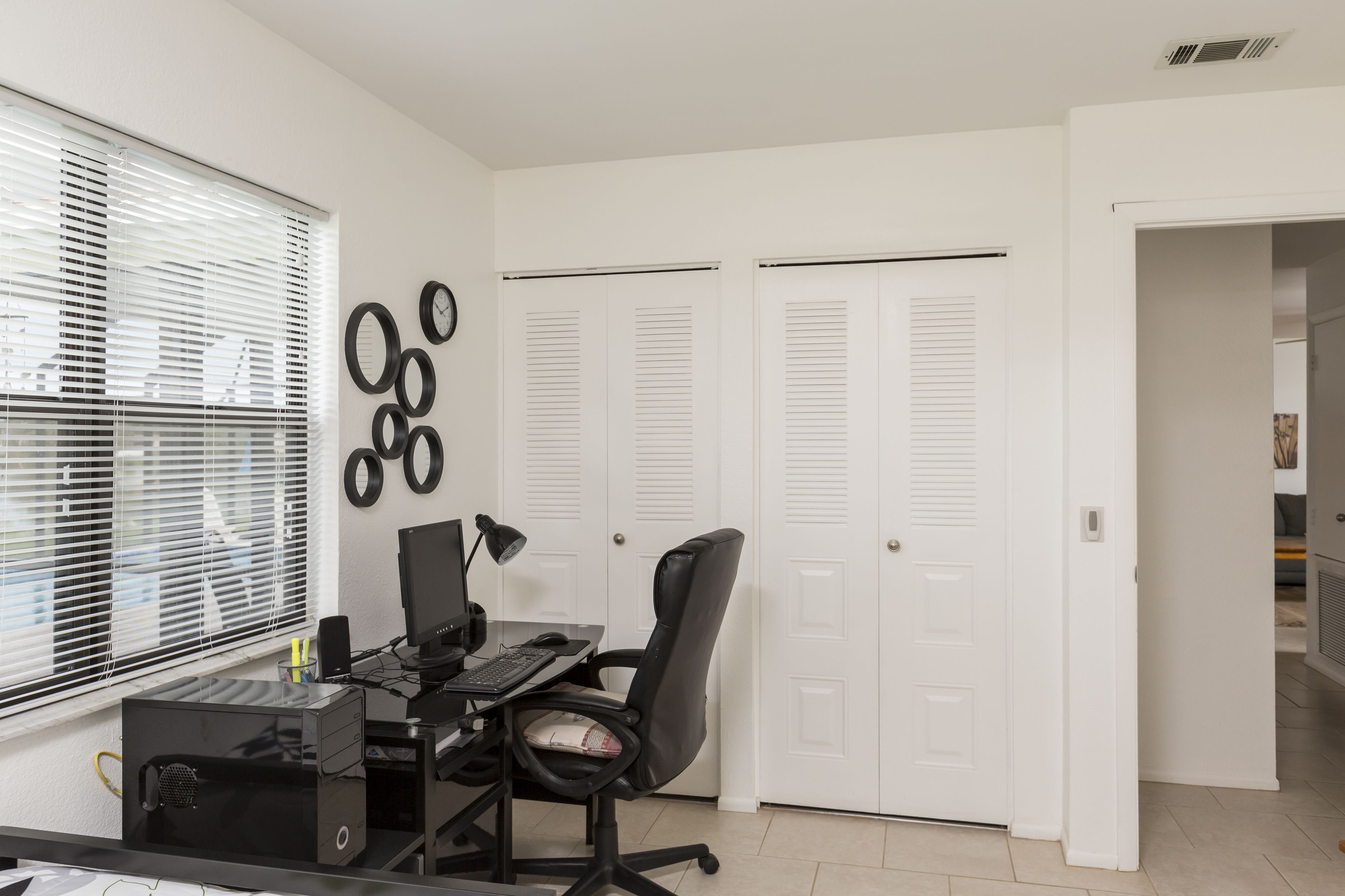 Un espace de bureau moderne avec un bureau, un ordinateur et une chaise. Les portes sont blanches et il y a une fenêtre avec des stores.