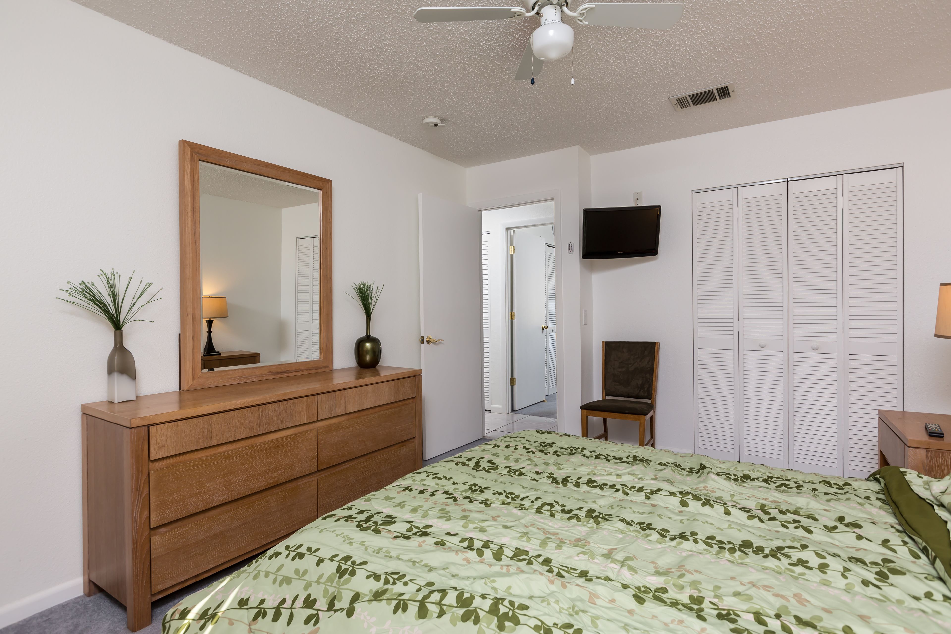 A bedroom with a bed, dresser, mirror, TV, and closet.