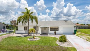 Une maison de plain-pied avec un porche couvert, un garage et une petite pelouse agrémentée d’un palmier.