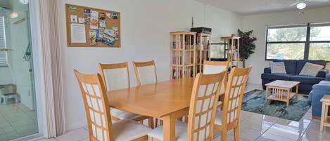 Een eethoek met een houten tafel en stoelen, een prikbord, een boekenkast en een blauwe bank.