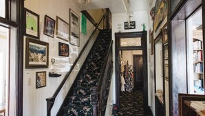 Un couloir avec un escalier, des tableaux encadrés accrochés aux murs et un sol recouvert d’une moquette.