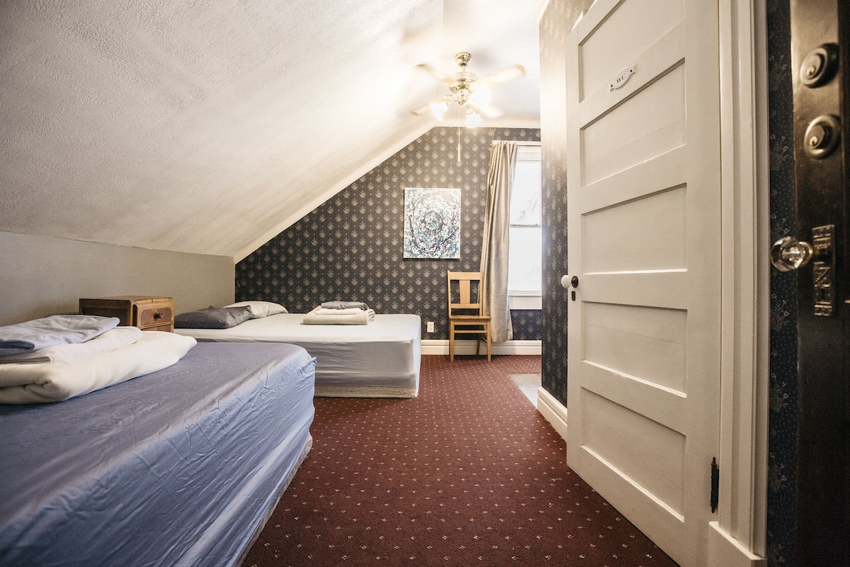 A bedroom with two beds, a ceiling fan, a window with curtains, and a door with a handle.