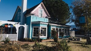 Un bâtiment à deux étages, à la façade bleue et blanche, doté d’une cheminée et d’un porche avec une clôture en treillis blanche.