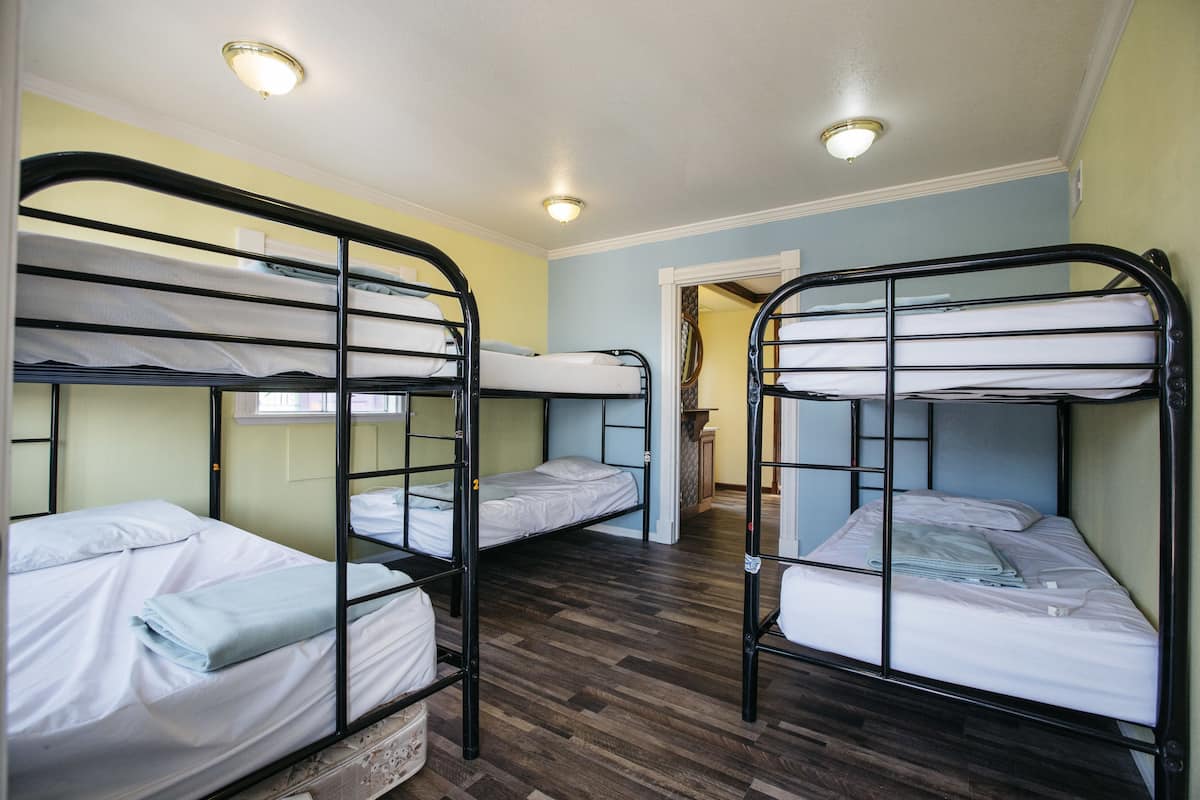 A dormitory room with bunk beds, wooden flooring, and a small window.