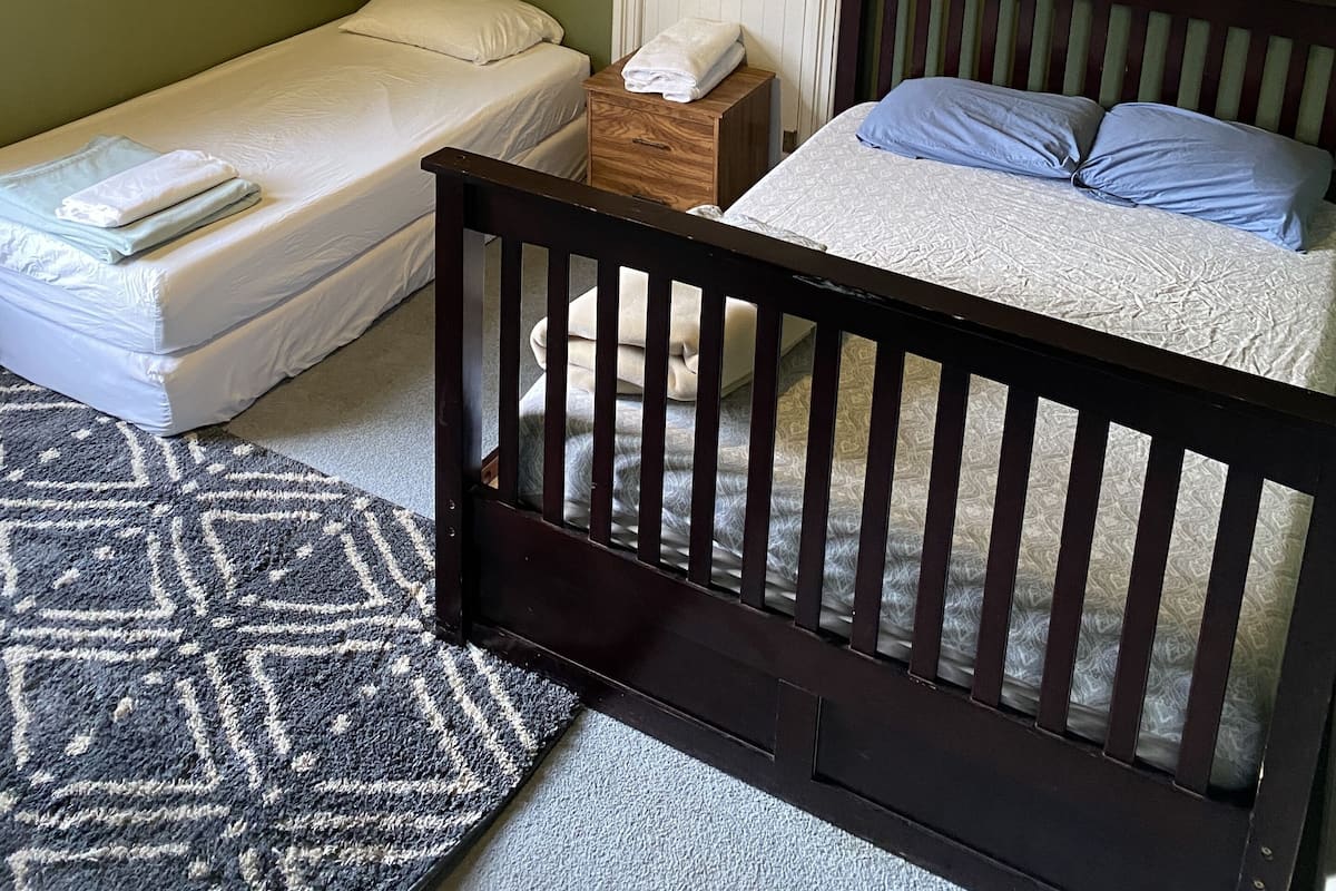 A bedroom with two beds, a wooden nightstand, a white door, a framed picture on the wall, and a ceiling light fixture.