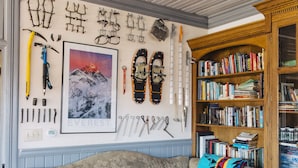 Une pièce chaleureuse avec un canapé vintage, une bibliothèque remplie de livres et un mur décoré d’équipements de ski et d’un tableau encadré.
