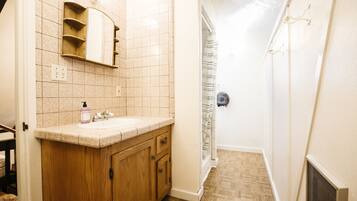 A bathroom with a wooden vanity, a sink, a mirror, and a shower area.