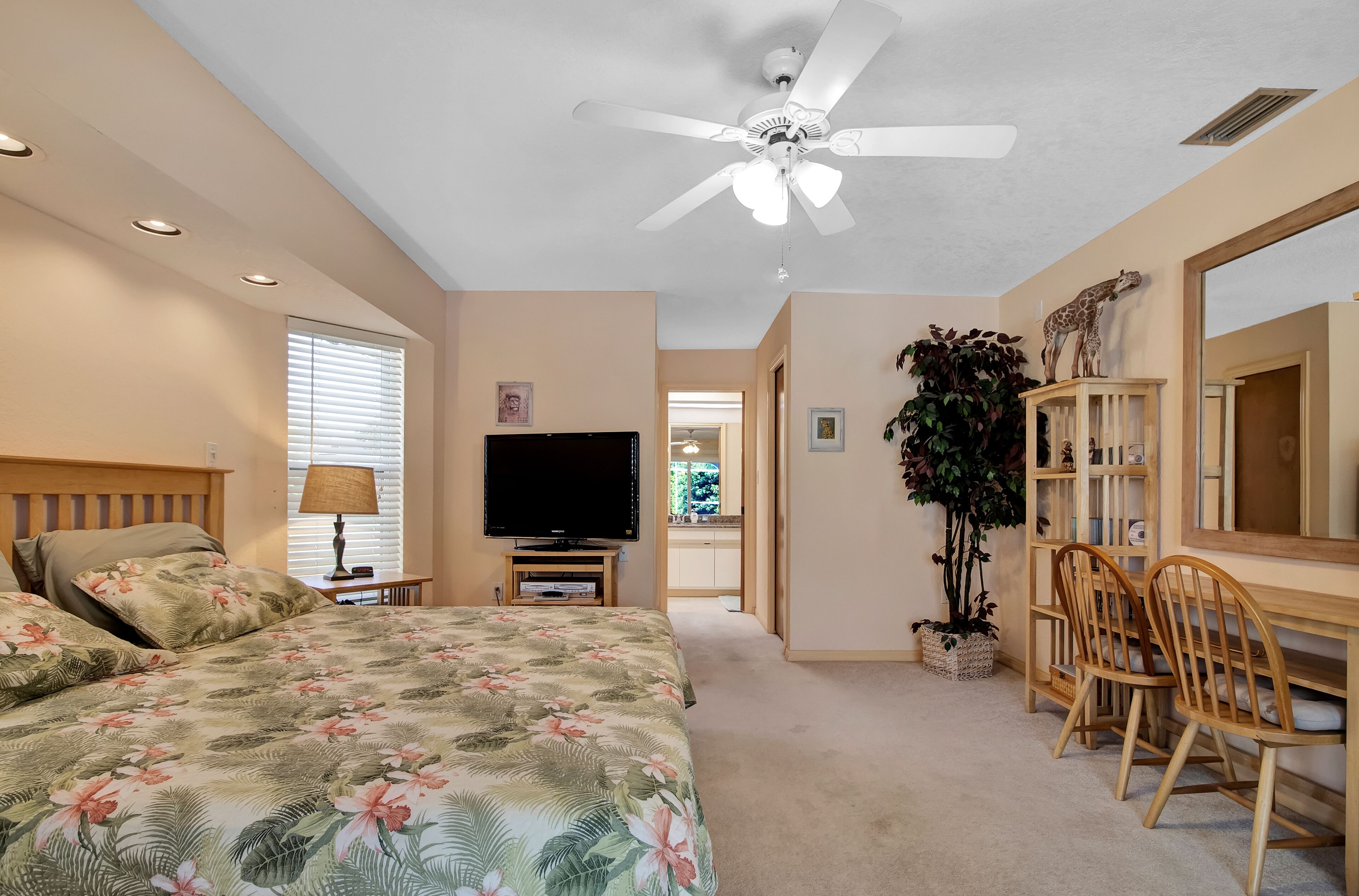 A bedroom with a bed, TV, ceiling fan, and a desk with chairs.