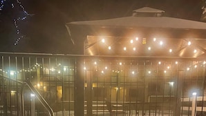 A snow-covered outdoor area with a hot tub, metal railing, and a building with string lights. - Timbers Motel (Bigfork)