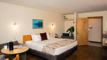 Habitación de hotel con cama, mesita de noche, lámpara de lectura y una pequeña zona de estar con una silla y una mesa.