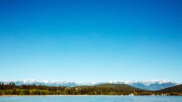 A lake with a forested shoreline and snow-capped mountains in the background.