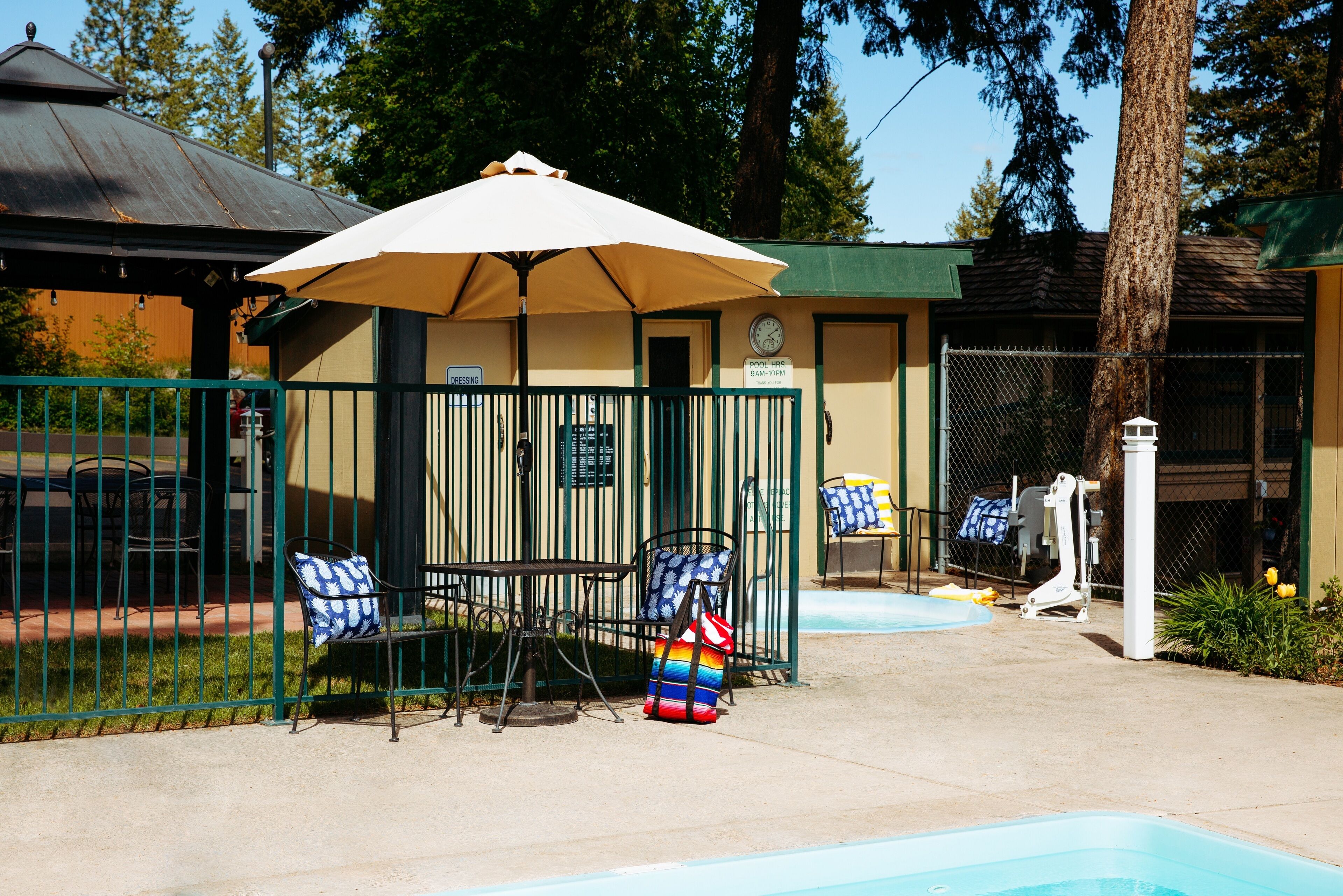 A pool area with a covered seating area, a fenced pool, and a building with a green roof.