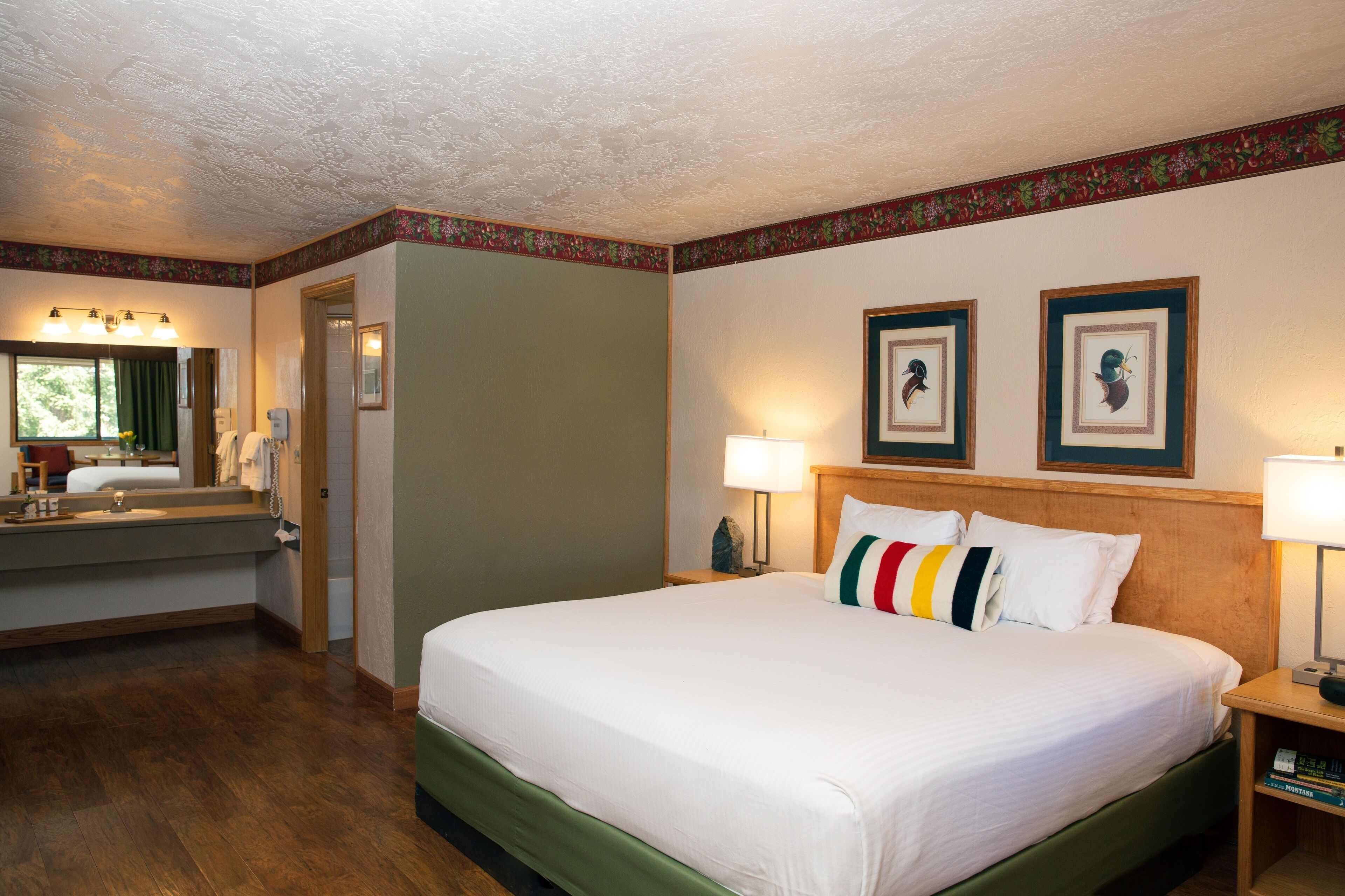 A hotel room with a large bed, a bathroom with a sink and mirror, and two framed pictures on the wall.