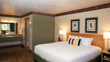 A hotel room with a large bed, a bathroom with a sink and mirror, and two framed pictures on the wall.