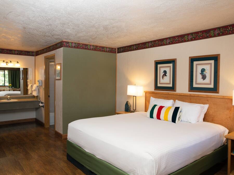 Ein Hotelzimmer mit einem großen Bett, einem Badezimmer mit Waschbecken und Spiegel sowie zwei gerahmten Bildern an der Wand.