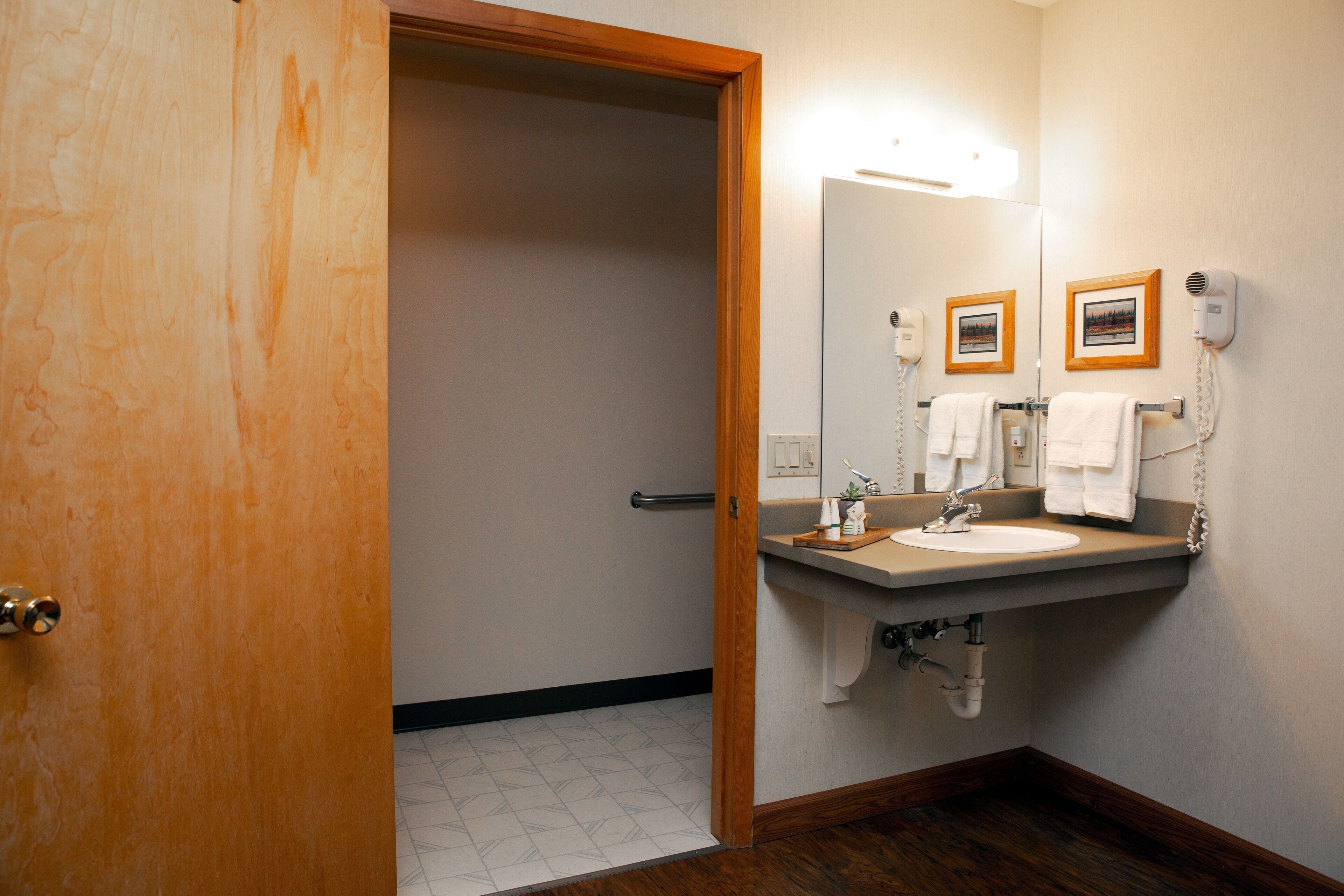 A bathroom with a wooden door, a sink with a mirror, a hairdryer, and a towel rack.