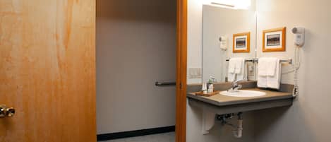 A bathroom with a wooden door, a sink with a mirror, a hairdryer, and a towel rack.