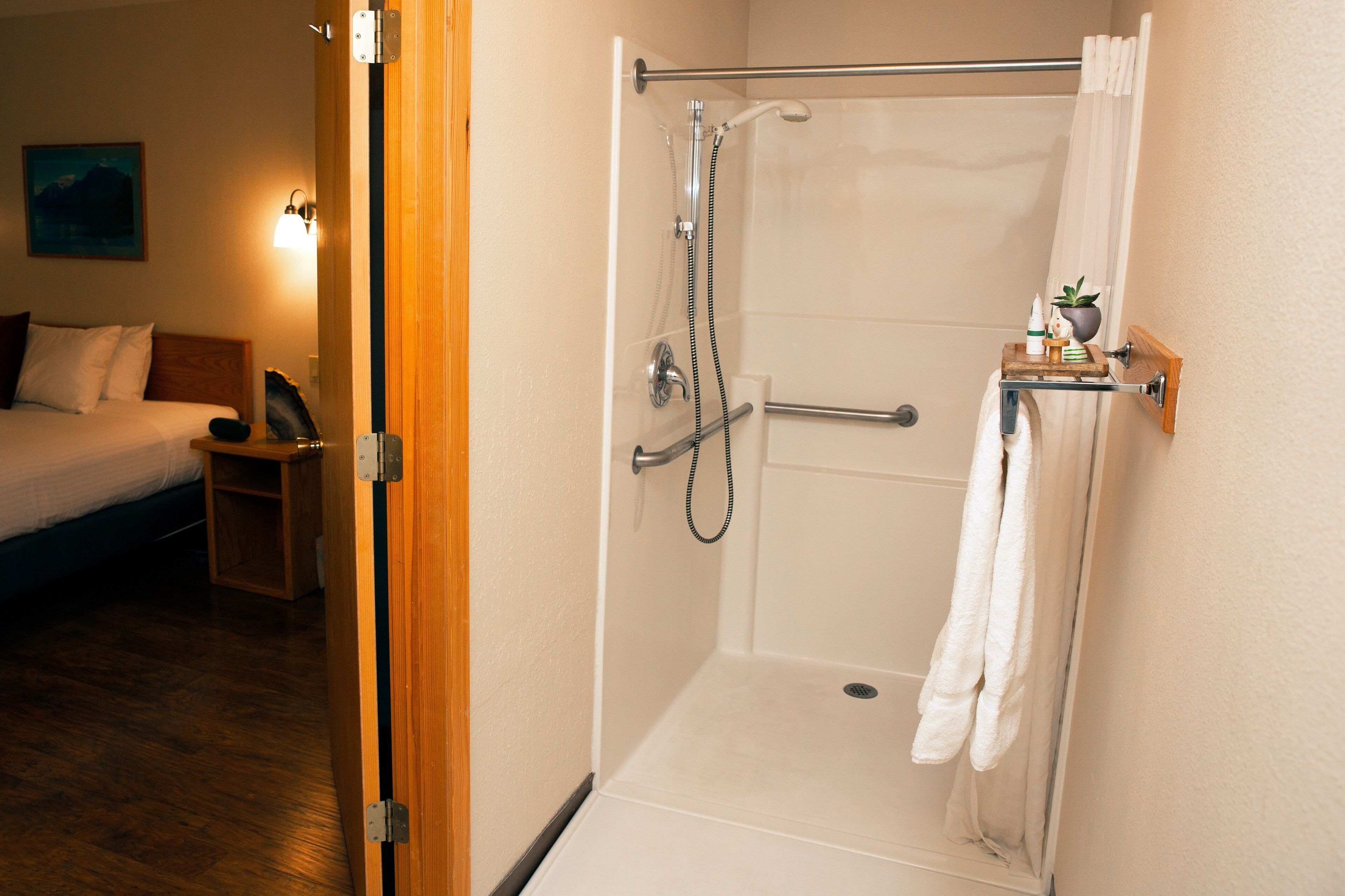 Un baño de hotel con ducha, inodoro y una mesita de noche con una toalla.