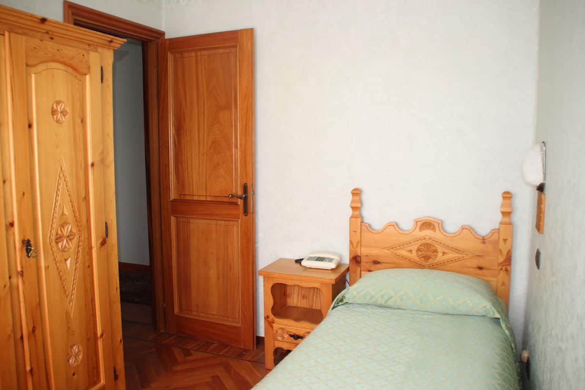 A bedroom with a wooden wardrobe, a bedside table with a phone, and a bed with a patterned bedspread.