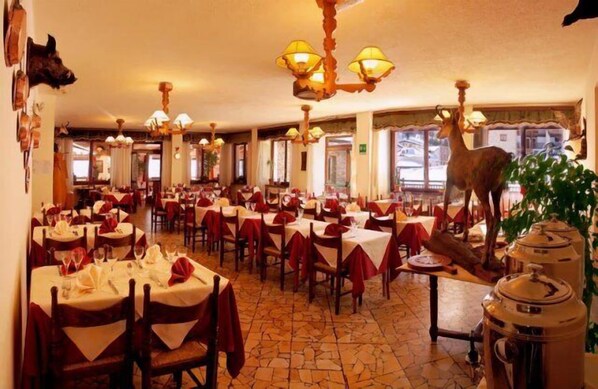 A restaurant with round tables, red tablecloths, and chandeliers. - Hotel Banchetta (Sestriere)