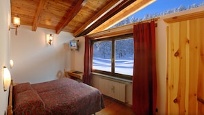 A bedroom with a bed, a wooden ceiling, a window with a view of a snowy landscape, and a television on the wall. - Hotel Banchetta (Sestriere)