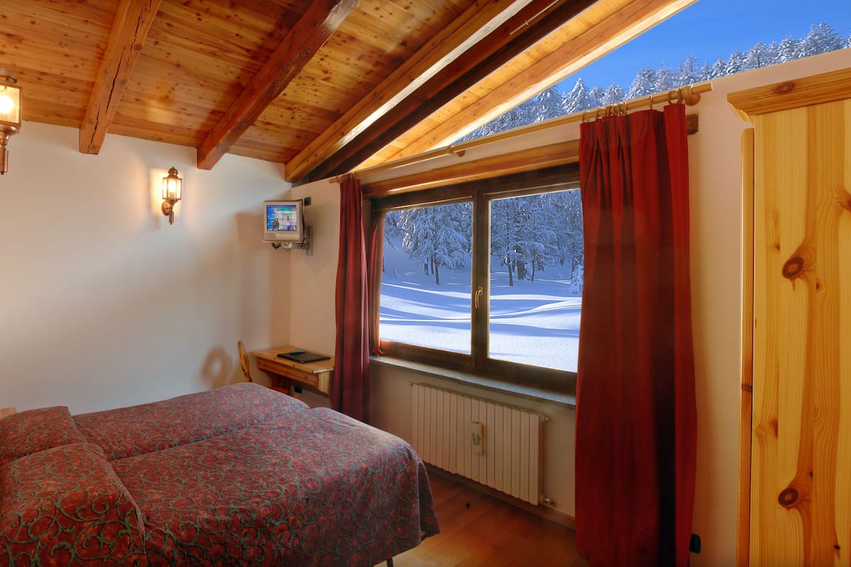 A bedroom with a bed, a wooden ceiling, a window with a view of a snowy landscape, and a television on the wall.