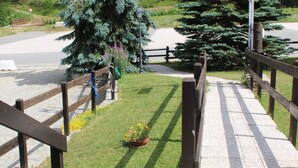 A paved walkway with wooden railings, surrounded by greenery and potted plants. - Hotel Banchetta (Sestriere)
