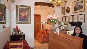 A hotel reception area with a wooden reception desk, a sofa, a dining table with chairs, and framed artwork on the walls. - Hotel Dalmazia (Florence)