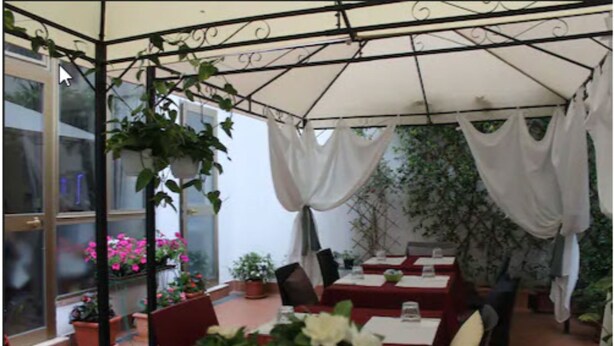A covered outdoor dining area with tables and chairs, potted plants, and a glass enclosure. - Hotel Dalmazia (Florence)