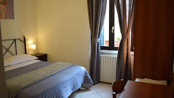 Un dormitorio con cama, mesita de noche, lámpara y vistas al exterior a través de cortinas.
