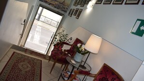 A room with a red patterned rug, wooden chairs, a table with a lamp, and a potted plant. - Hotel Dalmazia (Florence)