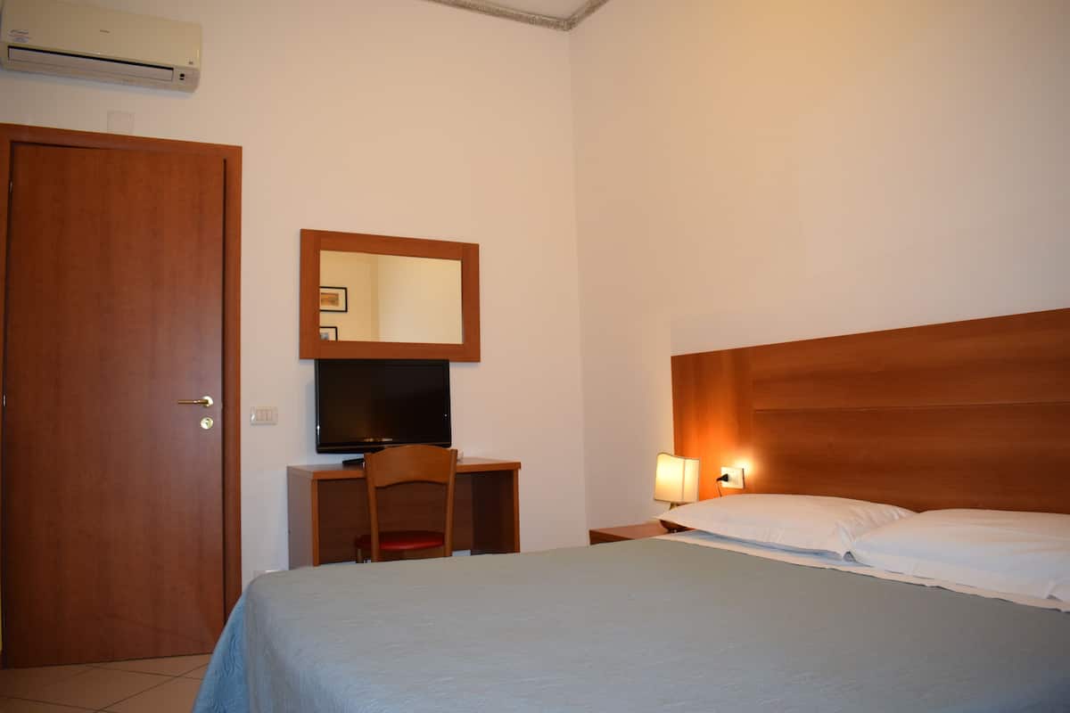 A hotel room with a bed, a desk with a chair, a television, and a wall-mounted mirror.