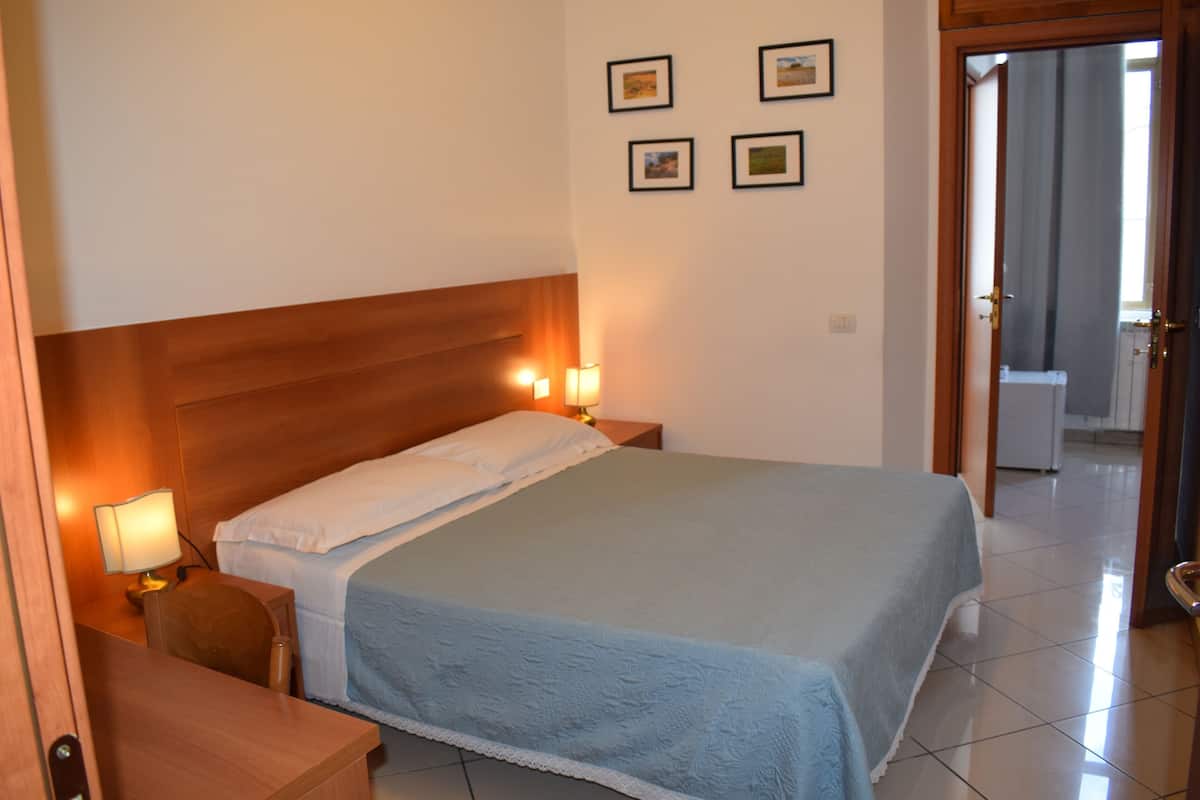 A hotel room with a bed, two bedside lamps, a wooden headboard, a nightstand, and a door leading to a bathroom.
