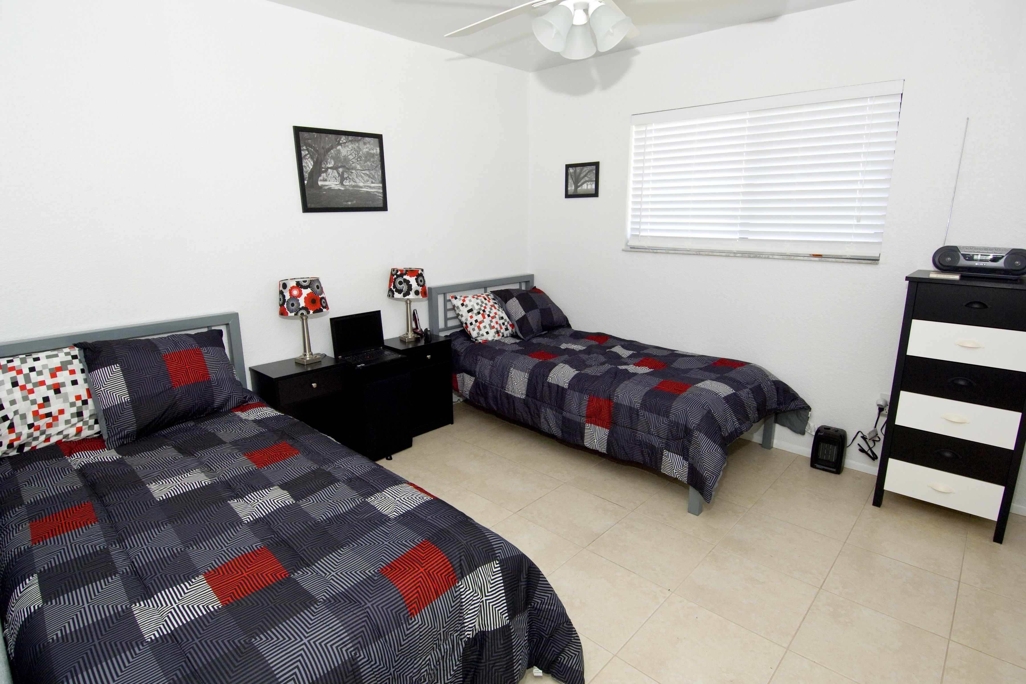 Un dormitorio con dos camas individuales, una mesita de noche, un aparador y un ventilador de techo.