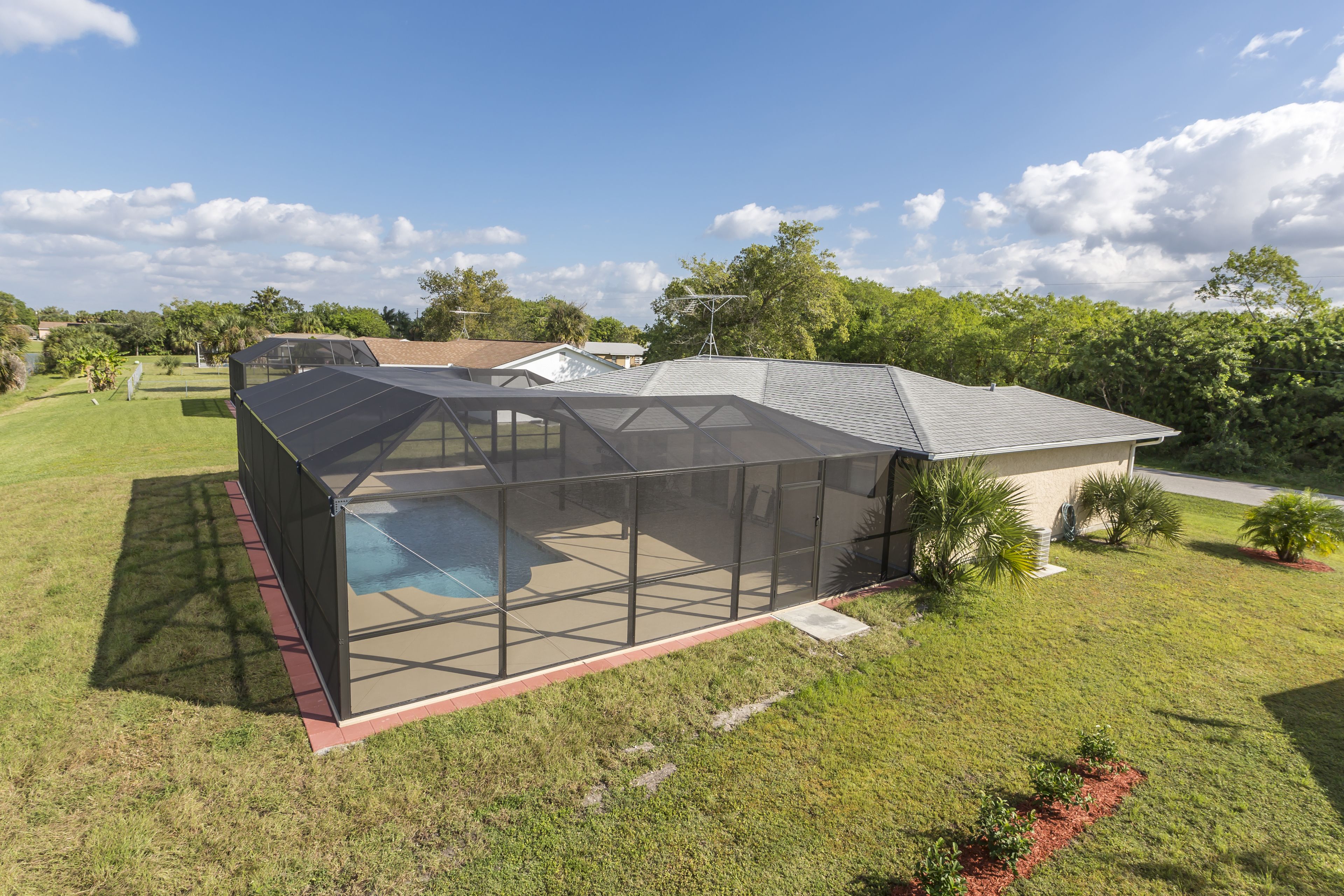 A modern house with a large glass-enclosed patio area, a swimming pool, and a well-maintained lawn.