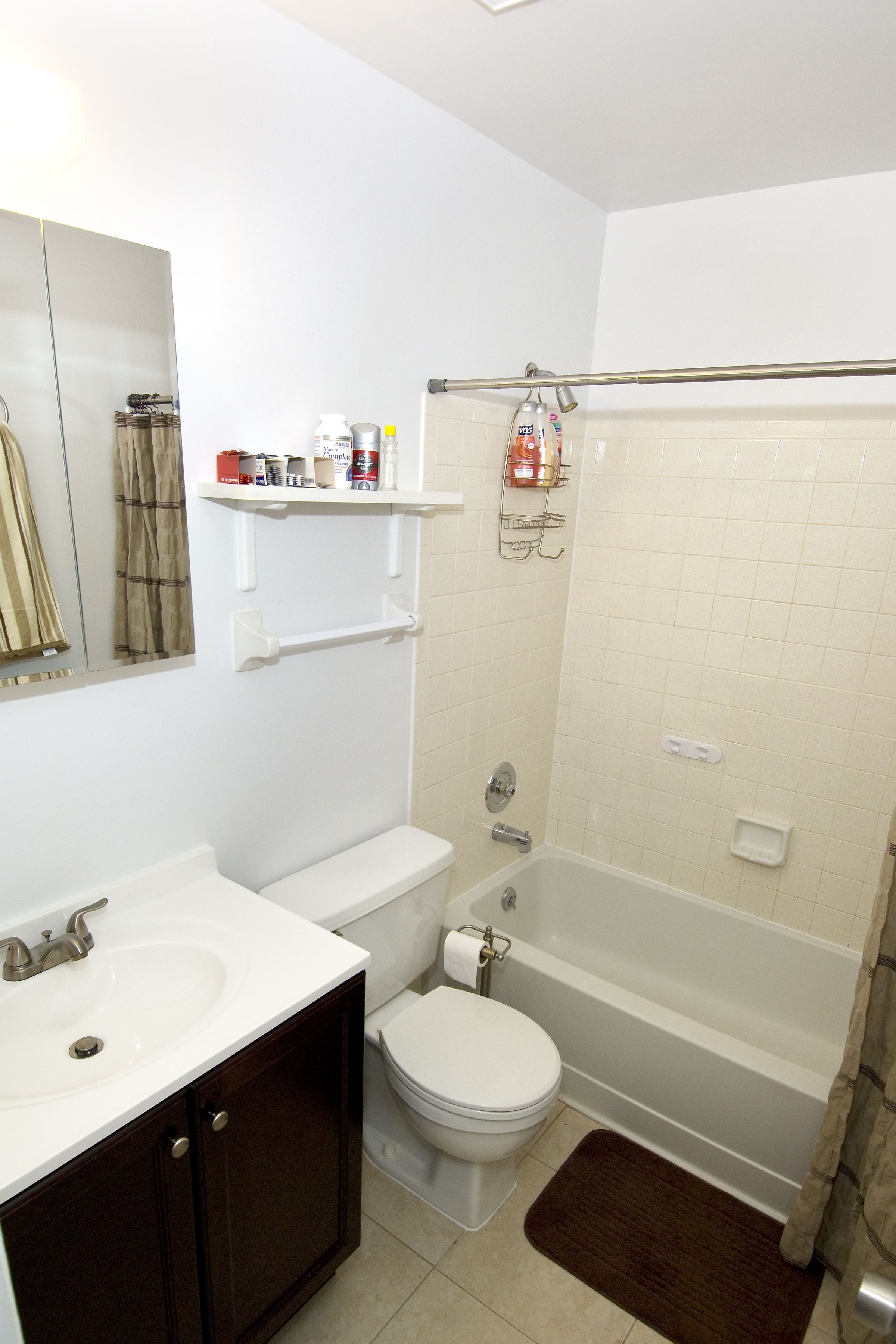 A bathroom with a toilet, sink, and bathtub. There are shelves above the toilet and a shower curtain.
