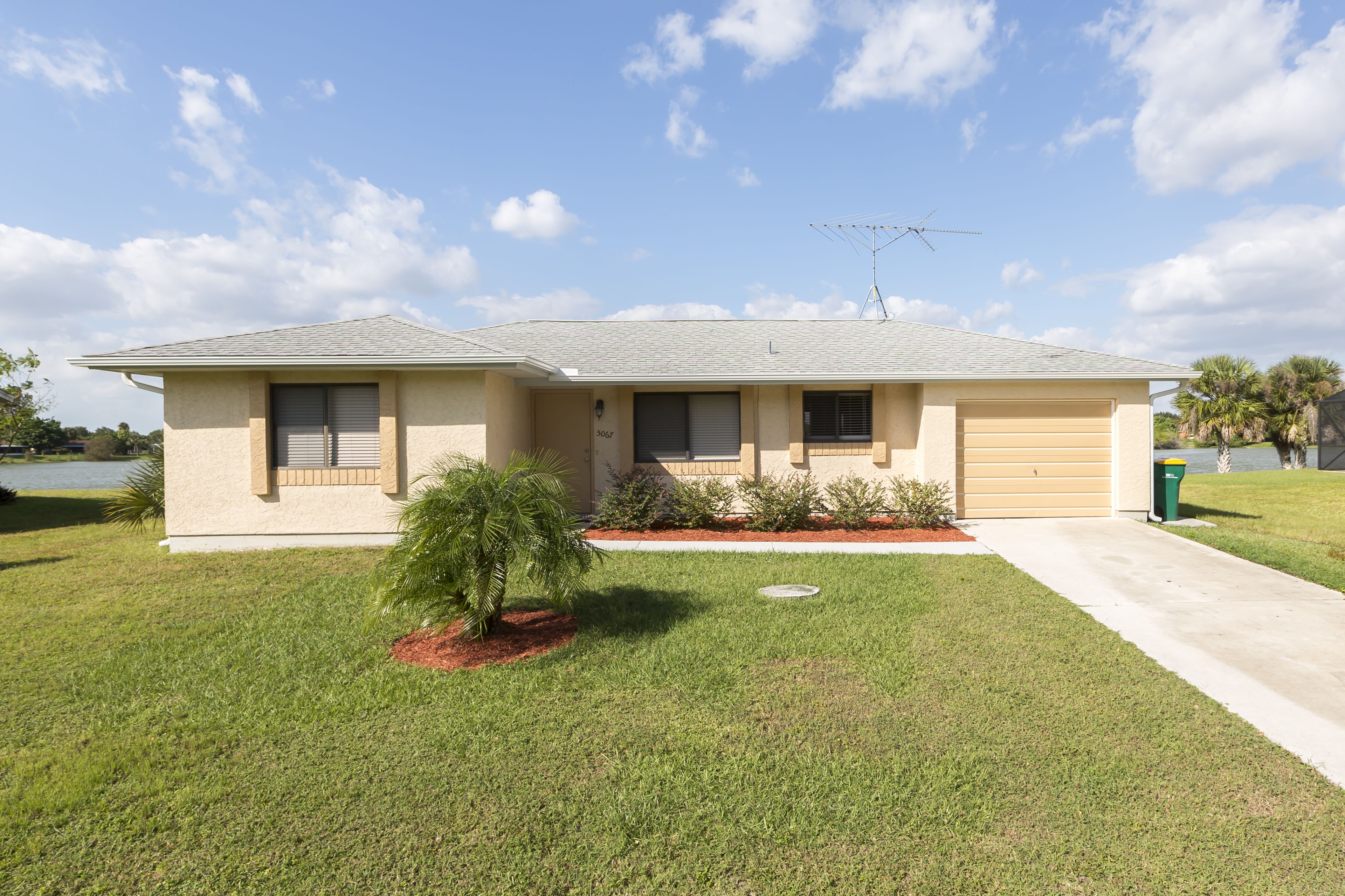 A single-story house with a garage, a small front yard with a palm tree, and a clear sky.