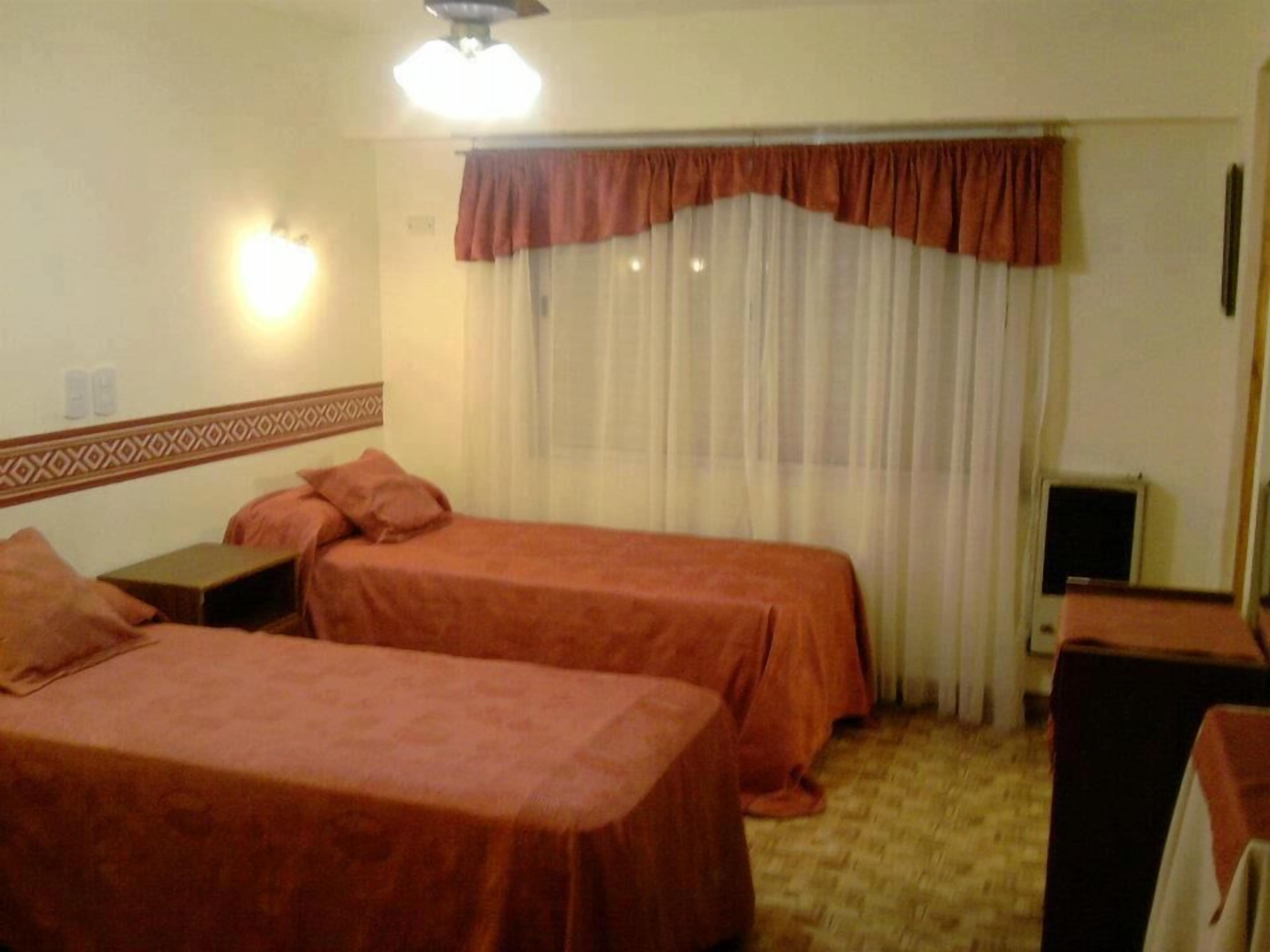 Habitación de hotel con dos camas individuales, un escritorio, una silla, un televisor y una ventana con cortinas.