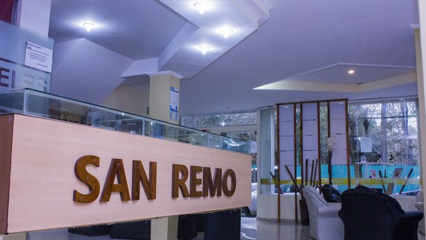 Un área de recepción con un letrero que dice 'SAN REMO', barandales de vidrio y una zona de estar con sillas.