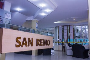 A reception area with a 'SAN REMO' sign, glass railings, and a seating area with chairs. - San Remo Majestic Hotel (Mar de Ajo)
