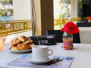 Une table avec des croissants, une tasse de thé et un vase décoratif contenant une fleur rouge.