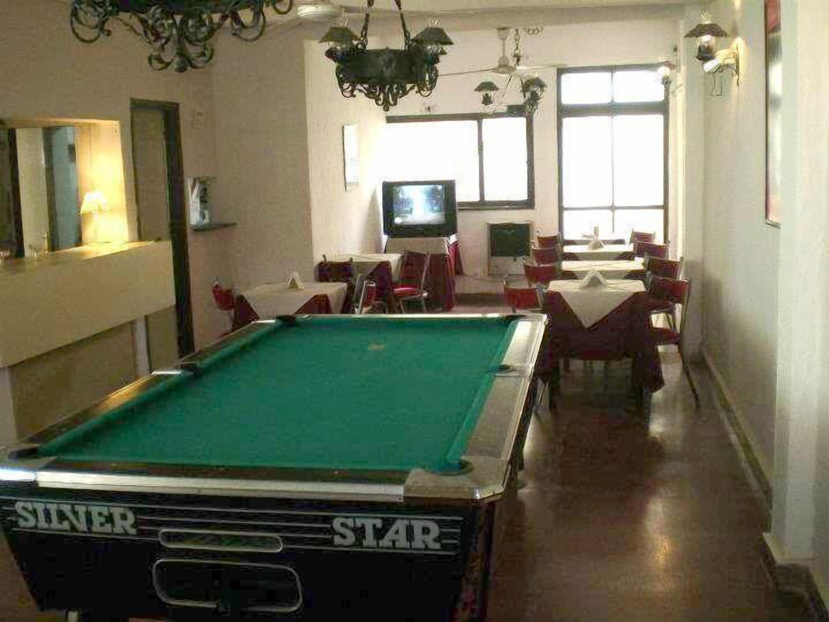 Una sala de billar con mesa de billar, sillas, televisor y ventana.