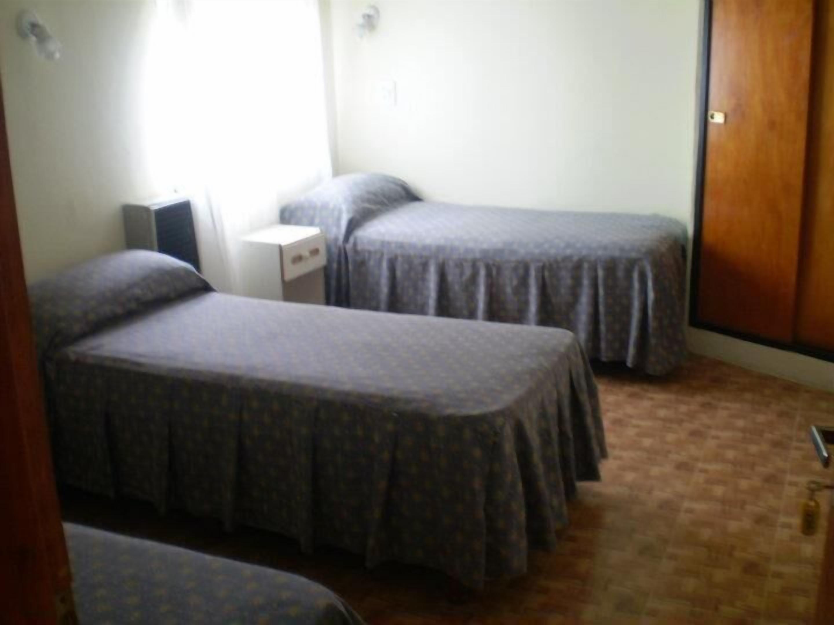 A room with two single beds, a small bedside table, a wardrobe, and a radiator.