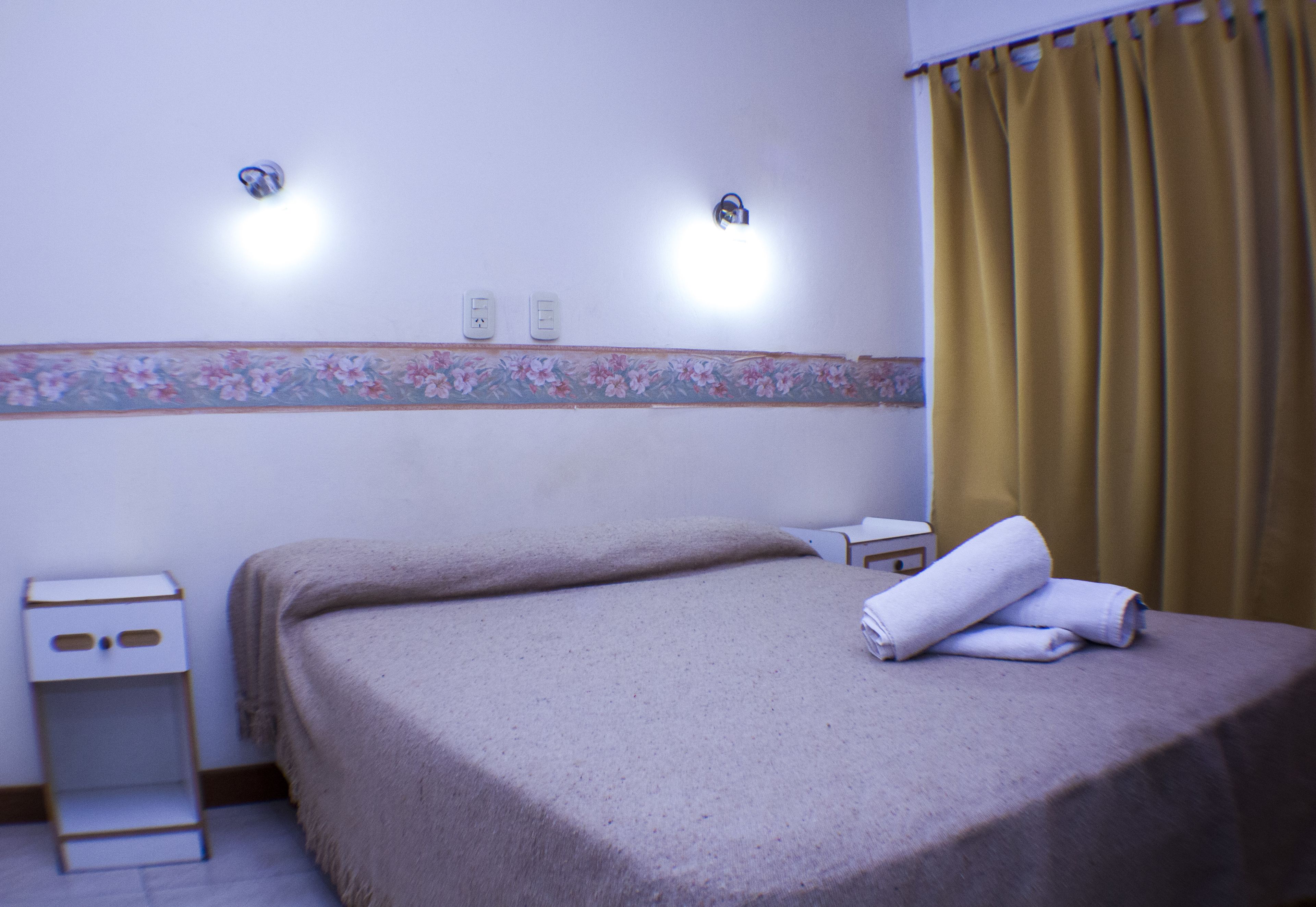 Una habitación de hotel con una cama, una mesita de noche y una lámpara fijada a la pared.