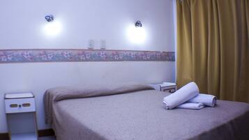 Una habitación de hotel con una cama, una mesita de noche y una lámpara fijada a la pared.